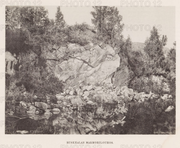 View of rocks by a body of water, Hämekoski. Ruskeala, page, photomechanical print, photographer: Impi Backman, cliché maker: anonymous, printer (person): Weilin & Göös, c. 1888 - c. 1893, printer (person), paper, autotypie, height 168 mm x width 225 mm, landscapes with waters, waterscapes, seascapes (in the temperate zone), rocks, Karelia, A grainy black-and-white photograph showing a rocky cliff face with large jagged boulders at its base and a reflective body of water in front, dense clusters of trees and shrubs growing atop and around the rock formation, a variety of tree shapes including tall slender trunks and bushier foliage, scattered smaller rocks and debris along the shoreline, and a clear sky above.