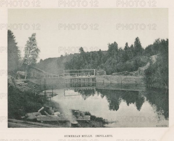 Sumerian Mylly. Impilahti, View of waterworks in a river, page, photomechanical print, photographer: Impi Backman, cliché maker: anonymous, printer (person): Weilin & Göös, c. 1888 - c. 1893, printer (person), paper, autotypie, height 161 mm x width 216 mm, trees, landscapes with waters, waterscapes, seascapes (in the temperate zone), Karelia, A sepia-toned riverside scene showing a wooden dam structure across calm water with its reflection visible, a dock and small boats moored near the bank, stacked logs and barrels on the shore, a simple wooden building and fences near the water, dense trees and foliage rising behind the structures, and a pale sky above.