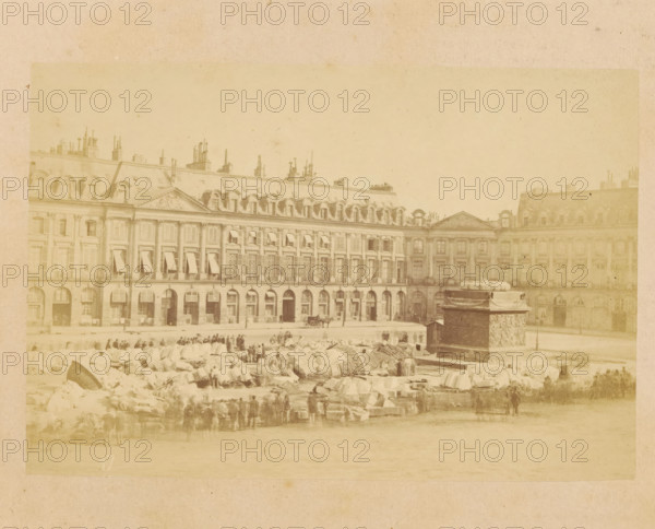 View of a demolished Colonne Vendôme, Colonne vendome Renversée, photograph, page, Place Vendôme, 1871, photographer, Paris, paper, albumen print, albumendruk, height 101 mm x width 150 mm, column, pillar, architecture, Place Vendome, A wide sepia-toned photograph shows a large multi-story classical building with arched ground-level openings, tall windows with shutters and awnings, and a mansard roof punctuated by numerous chimneys and dormer windows; in front of the building a plaza contains a stone fountain base with sculpted reliefs and a pile of large stone blocks and rubble, with small groups of people standing and walking among the stones and a horse-drawn carriage visible near the building.