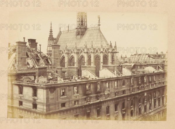 View of a destroyed Palace of Justice in Paris, Ensemble du Palais de Justice, photograph, page, 1871, photographer, paper, albumen print, albumendruk, height 101 mm x width 151 mm, ruin of a dwelling, house, castle, palace, Paris, Palais de Justice, A sepia-toned photograph shows the upper facade and roofline of a large stone building with Gothic architectural elements, including pointed arches and ornate tracery on tall windows beneath a steeply pitched roof with decorative pinnacles and a slender spire. The roof and parts of the upper walls appear damaged, with exposed beams, rubble, and partial collapses revealing interior spaces and broken masonry. Chimneys and rooftop structures rise above the ruined sections, and the row of rectangular windows on the building's lower stories shows soot-darkened frames and broken panes. In the background, additional rooftops and architectural details are visible against a pale sky.
