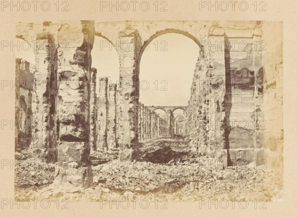Grenier d'Abondance - vue intérieure, View of the interior of a destroyed building, photograph, page, 1871, photographer, paper, albumen print, albumendruk, height 101 mm x width 151 mm, ruin of a dwelling, house, castle, palace, Paris, A sepia-toned photograph of a long colonnade of stone arches and pillars seen from ground level, with rough, weathered stone surfaces and fractured edges, rubble scattered across the floor, light filtering through the open archways, multiple repeating arches receding into the distance, large vertical stone supports on either side, and a narrow view down the central aisle framed by the tall curved arch in the foreground.