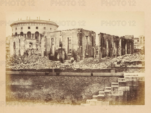 Docks de la Vilette, View of a destroyed building, photograph, page, 1871, photographer, paper, albumen print, albumendruk, height 101 mm x width 151 mm, ruin of a dwelling, house, castle, palace, A sepia photograph showing a row of damaged stone buildings with large rectangular window openings and rough, crumbling facades, piles of rubble and debris scattered along their bases, and a rounded multi-story structure with arched openings and a colonnade visible behind them, a low stone wall running across the foreground, and a stepped stone stairway descending at the right edge of the image.