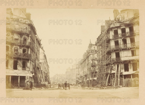 Rue de Rivoli, View of destroyed buildings on Rue de Rivoli, photograph, page, Paris, 1871, photographer, paper, albumen print, albumendruk, height 101 mm x width 151 mm, street, theater (building), A sepia-toned street scene showing tall multi-story buildings on both sides with façades featuring balconies and window openings, many of which are damaged or empty, and wooden scaffolding and beams leaning against and supporting several of the buildings; in the foreground a cobbled street leads toward the background where a few horse-drawn carts and figures are visible near the center, flanked by piles of debris and construction materials along the sidewalks, with distant buildings fading into the light sky above.