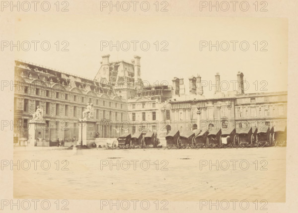 Palais des Tuileries - vue extérieurre, View of the destroyed Tuileries Palace in Paris, photograph, page, Tuileries Palace, 1871, photographer, Paris, paper, albumen print, height 101 mm x width 150 mm, ruin of a dwelling, house, castle, palace, A wide pale photograph of an ornate stone building with rows of arched windows and decorative roofline elements, including sculpted figures and ornamental pediments, a central section with a steeply pitched roof and scaffolding or exposed framework, and several tall chimneys and vertical architectural features along the roof. In front of the building a fenced courtyard contains a series of covered horse-drawn carriages lined up side by side, lamp posts, and two large sculpted statues mounted on tall pedestals near the entrance. The foreground shows a broad open paved area with faint shadows and some indistinct figures and blurs suggesting movement.