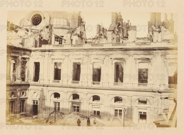 Palais Royal, View of the ruined Palais Royal, photograph, page, Palais-Royal, 1871, photographer, Paris, paper, albumen print, albumendruk, height 101 mm x width 151 mm, ruin of a dwelling, house, castle, palace, A sepia-toned photograph of a large multi-story stone building with classical architectural details showing extensive damage and missing windowpanes, with an upper section where rooflines and chimneys are jagged and partially collapsed, a circular window opening near a dome, decorative columns and balustrades along the facade, several arched openings on the lower level and tall rectangular window openings above, rubble piled against the base of the building, a single street lamp in front of the facade, and four small human figures standing near the rubble.