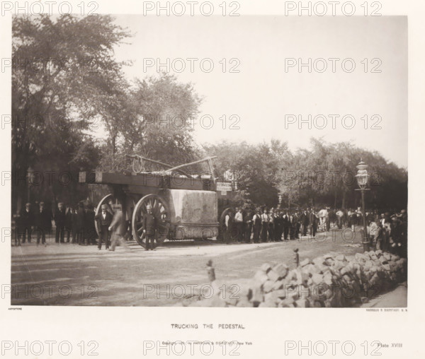Trucking the pedestal, page, photomechanical print, inscription: 'Copyright 1881, by HARROUN & BIERSTADT, New York', number: 'Plate XVIII', New York, cliché maker: Harroun & Bierstadt (possibly), 1880, photographer, printer (person), North America, paper, collotype, artotype, height 189 mm x width 255 mm, (farm) wagon, freight wagon, cart, obelisk, needle, base (, column, pillar), A large wooden wagon with oversized wooden wheels stands in a tree-lined street, its flatbed carrying a block-shaped stone pedestal and long timber beams with ropes and chains draped over them; a crowd of men in dark suits and hats stands around and alongside the wagon, with some men positioned near the wheels and others in a line behind it, while horses and additional figures are visible further back; tall gas-style street lamps rise near the roadside and a low stone wall runs along the foreground, with leafy trees forming a backdrop and open sky filling the upper part of the image.