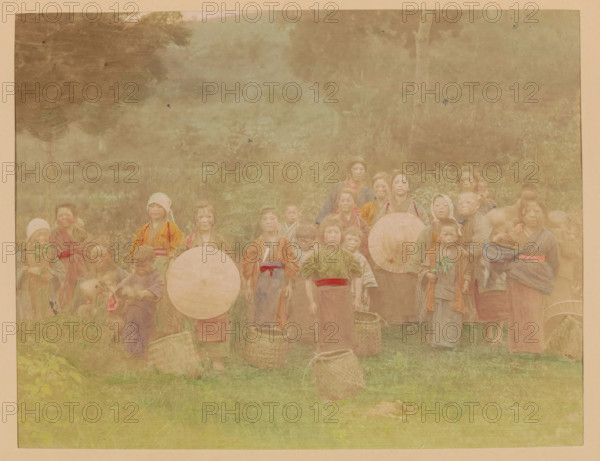 Group portrait of tea pickers, photograph, page, Japan, c. 1887 - in or before 1897, photographer, colorer (graphic design artist), paper, albumen print, hand coloring, photographie peinte, height 187 mm x width 244 mm, Photo for page 195., working class, labourers, anonymous historical persons depicted in a group, in a group-portrait, child labor, A faded group portrait of people standing outdoors in front of trees and foliage, many wearing traditional clothing and head coverings in muted colors, several holding round umbrellas and woven baskets at their feet, with children and adults arranged across the width of the scene and a grassy foreground.