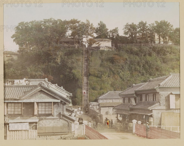 View of the hundred-step staircase in Yokohama, photograph, page, Japan, c. 1887 - in or before 1897, photographer, colorer (graphic design artist), paper, albumen print, hand coloring, photographie peinte, height 188 mm x width 245 mm, Photo for page 241., street, façade (of house or building), staircase, A street scene with traditional tiled rooftops in the foreground, a narrow path between buildings leading toward a steep grassy hillside, and a long wooden stairway ascending the hill flanked by vegetation and trees at the top; wooden and plaster buildings line the street with windowed facades and awnings, a few people stand and walk along the street near carts and a horse, one person wears a bright garment that contrasts with the muted tones, and trees and small structures sit along the ridge above the stairway.