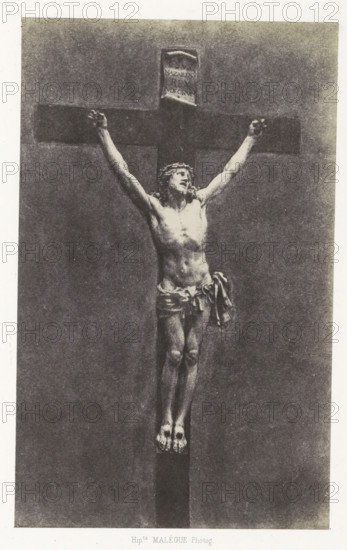 Ivory crucifix from the cathedral of Le Puy, Christ en ivoire, photograph, page, inscription: 'appartenant a la cathédrale du Puy.', number: 'PL. 19.', photographer: Hippolyte Malègue, France, c. 1850 - in or before 1857, paper, salted paper print, height 200 mm x width 124 mm, sculpture, the crucifixion of Christ: Christ's death on the cross, Golgotha (Matthew 27:45-58, Mark 15:33-45, Luke 23:44-52, John 19:25-38), A monochrome image of a crucifix with a carved figure of a man affixed to a dark wooden cross, the figure shown full length with arms outstretched and hands positioned at the ends of the horizontal beam, a loincloth draped around the waist with fabric folds hanging at one side, a crown-like headpiece on the head and a tilted facial expression, a visible torso with muscular definition, legs together and feet resting on a small platform at the base of the vertical beam, a small rectangular plaque above the head attached to the top of the cross, and an even textured background...