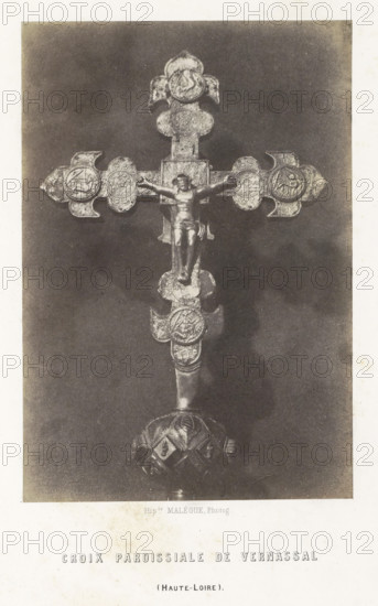 Parochial cross from Vernassal, Croix paroissiale de Vernassal, photograph, page, number: 'PL. 6.', inscription: '(Haute-Loire).', photographer: Hippolyte Malègue, France, c. 1850 - in or before 1857, paper, salted paper print, height 193 mm x width 133 mm, crucifix, personal devotion, A photographic image of an ornate metal cross with a central figure of a crucified person mounted on a dark rectangular background; the cross has decorative round medallions at the ends and along the shaft, each containing intricate embossed designs, and the base of the cross shows a rounded, patterned support.