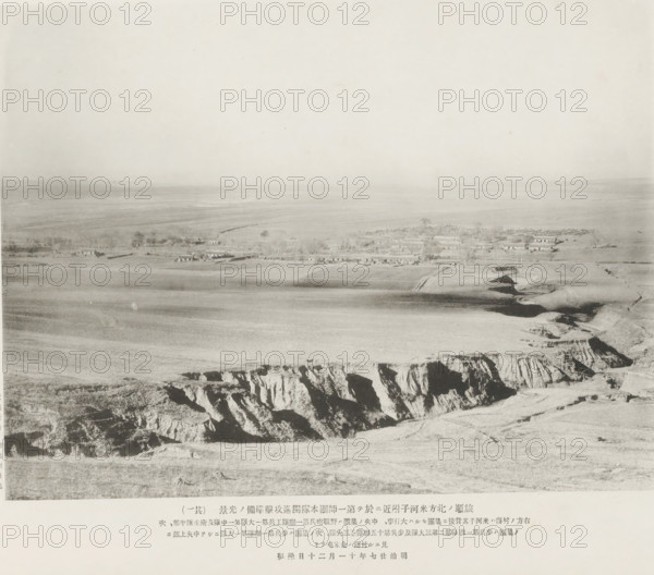 Preparations for advance and attack being made by the main body of the first division near Mehotse, N. of Port Arthur, page, photomechanical print, inscription: 'The village to the right is Mehotse, The village seen higher up in the center is Kinheatun.', inscription: 'The fall of Port Arthur.', photographer: Ordnance Survey, Manchuria, cliché maker: Kazumasa Ogawa, Japan, 1894-11-20, paper, collotype, photoprint, height 201 mm x width 265 mm, city-view in general, 'veduta', A wide, pale landscape photograph showing a flat plain stretching to the horizon with a small cluster of low buildings and trees near the middle ground, lighter fields and furrows in front of them, and a rugged cliff edge with deep vertical rock faces in the foreground.