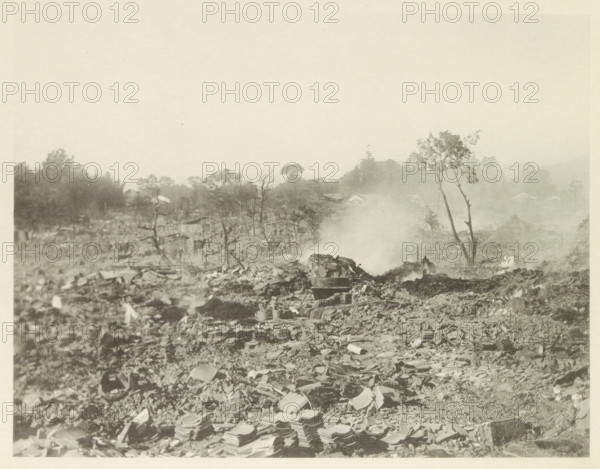 Destroyed buildings in Kasamatsu after an earthquake, page, photomechanical print, Kasamatsu, cliché maker: Kazumasa Ogawa, Japan, after 1891-10-28 - in or before 1892, photographer, Chubu, Gifu, paper, collotype, photoprint, height 216 mm x width 281 mm, ruin of a building, architecture, consequences of an earthquake, Mino–Owari earthquake 1891, A wide, sepia-toned scene of rubble and debris stretching toward a hazy horizon, with broken roof tiles and scattered stones in the foreground, low smoke or mist rising near the center, sparse leafless and partially leafed trees standing among the ruins, distant treeline and faint building shapes behind the haze, and an overall flat, dusty landscape under a pale sky.