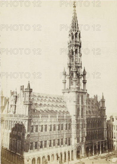 Town Hall of Brussels, Bruxelles - Hôtel-de-ville, photograph, page, name: '(Phot. de Brand frères, rue de la Madeleine, 32.)', photographer: Brand Frères, Brussels, c. 1862 - c. 1872, paper, albumen print, height 205 mm x width 151 mm, Photo on page 19., town hall, façade (of house or building), Stadhuis (Brussels), A large ornate stone building fills the image, featuring a tall, intricately detailed spire rising above a multi-story façade. The façade displays rows of arched windows and decorative stonework, including columns, statues, and carved patterns. One section shows a steep roof with a series of small dormer windows, and several turrets and pinnacles punctuate the roofline. At street level there are large archways and entrances, and a few small figures and horse-drawn vehicles are visible near the building's base. The photograph has a pale, aged tone with high contrast between the building details and an empty sky.