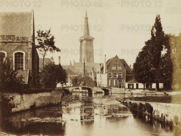 Bruges, View of the Minnewater in Bruges, photograph, page, c. 1862 - c. 1872, photographer, paper, albumen print, albumendruk, height 147 mm x width 193 mm, Photo on page 33., pond, pool, tower, clock tower, monumental adornment, A sepia-toned view of a canal with still water reflecting parts of the scene, a stone arched bridge crossing the canal, rows of old brick buildings with tiled roofs along the water, a tall church tower with a pointed spire rising behind the rooftops, trees of varying heights framing the scene, and a large building with arched windows visible on the left.