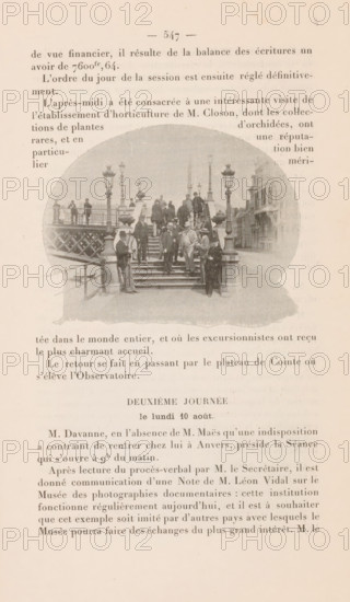 Members of the Union International de Photographie on a staircase in Liège, page, photomechanical print, 1896, paper, autotypie, height 67 mm x width 90 mm, historical persons (portraits and scenes from the life), staircase, A faded page with printed columns of text surrounding a central oval photograph showing a group of people standing and sitting on a set of stone steps leading up to a bridge or elevated walkway; the photograph includes decorative lamp posts and railings, several men in period clothing and hats clustered on the stairs and landing, a few figures standing on the bridge beyond, and buildings visible along a street to the right; the page has a worn, yellowed appearance and the photograph is slightly grainy and washed out.