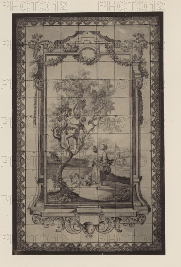 Tile wall of apple picking in the house of Antonin Terme, photograph, page, Liège, c. 1880 - in or before 1885, photographer, paper, platinum process, height 210 mm x width 133 mm, interior of the house, art collection, art gallery, tiles, bricks, building material, A tall rectangular artwork composed of square tiles framed by a patterned border is visible. The central scene shows a leafy tree with a figure perched among its branches and a standing figure nearby reaching upward while holding a wide-brimmed hat and a basket-like object. At the base of the tree two smaller figures sit on the ground near a basket. Architectural elements resembling columns and ornate scrollwork frame the central image, with decorative flourishes along the top and bottom margins. The image is monochromatic with shading that defines foliage, figures, and ornamental details, and faint grid lines where the tiles meet are visible across the entire surface.