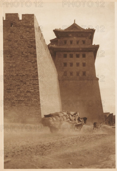 Cart pulled by a horse near a building, page, photomechanical print, photographer: Donald Mennie, Beijing, cliché maker: anonymous, c. 1915 - in or before 1920, paper, rotogravure, height 276 mm x width 191 mm, two-wheeled, animal-drawn vehicle, civic architecture, edifices, dwellings, A tall brick wall rises along the left side of the image next to a multi-tiered tower with eaves and small square openings, both rendered in a monochrome sepia tone; at the base of the structures a cart loaded with rounded sacks is being pulled by an animal, and another animal stands nearby, while dust or haze swirls around their legs and the foreground shows a textured, dusty ground.