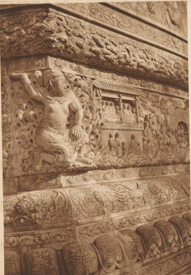 Detail of a stupa, page, photomechanical print, photographer: Donald Mennie, Beijing, cliché maker: anonymous, c. 1915 - in or before 1920, paper, rotogravure, height 279 mm x width 196 mm, statues, paintings, etc., objects of worship (non-Christian religions), A close view of an ornate carved stone relief showing a seated figure with one arm raised and the other resting on a knee, surrounded by swirling cloud-like and floral patterns, with a rectangular niche containing smaller seated figures and standing attendants, bordered by decorative bands and layered carved moldings, all rendered in a monochrome sepia tone.
