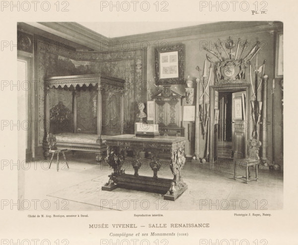 View of a room with Renaissance art in the Musée Antoine Vivenel in Compiègne, France, Musée Vivenel - Salle Renaissance, Compiègne et ses Monuments (oise), page, photomechanical print, inscription: 'Reproduction interdite.', number: 'Pl. IV.', maker: Jules Royer, Compiègne, maker: Augustin Boutique, Douai, c. 1890 - in or before 1895, paper, collotype, photoprint, height 123 mm x width 172 mm, Print on second unnumbered page after page 4., permanent exhibition, museum, furniture and household effects, A photograph of an interior room showing ornate antique furniture and wall decorations, including a large canopy bed with carved posts and a detailed headboard partially covered by patterned tapestries, a heavy carved table with ornate legs in the foreground, a small decorative stool with turned legs, and a chair with a carved back at the right; on the right wall there is an arrangement of swords and polearms fanning out above a decorative crest and a doorway that reveals another room wi...