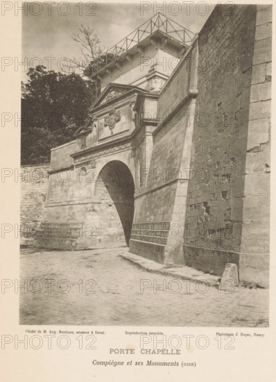 View of a chapel door in Compiègne, France, Porte Chapelle, Compiègne et ses Monuments (oise), page, photomechanical print, number: 'Pl. VIII.', inscription: 'Reproduction interdite.', maker: Jules Royer, Compiègne, maker: Augustin Boutique, Douai, c. 1890 - in or before 1895, paper, collotype, photoprint, height 160 mm x width 124 mm, church (exterior), by, A sepia-toned photograph shows a stone archway set into a large masonry wall with a sloping buttress beside it; above the arch is an ornate pediment with sculpted decoration and moulded cornices, and a heavy stone façade with architectural details. The cobbled ground in front of the arch slopes slightly and meets the base of the wall. To the left of the arch a lower stone wall and dense foliage with tall trees are visible, and a bare-branched tree rises behind the structure. The right side of the image is dominated by a tall, textured stone wall with visible joints and weathering, and the upper portion of the scene shows a flat-roo...