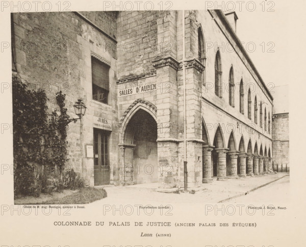 Colonnade du Palais de Justice (Ancien Palais des Évêques), View of a colonnade of the courthouse of Laon, France, Laon (Aisne), page, photomechanical print, inscription: 'Reproduction interdite.', number: 'Pl. V.', maker: Jules Royer, maker: Augustin Boutique, Douai, c. 1891 - in or before 1896, paper, collotype, photoprint, height 118 mm x width 169 mm, Print on third unnumbered page after page 4, colonnade, court building, A sepia-toned photograph of a stone building featuring an arched colonnade along one side and a corner entrance with a pointed arch, fluted columns supporting the arches, rectangular windows with pointed tops on the upper level, a vertical downspout running along the corner, a wall-mounted lantern beside a doorway, climbing foliage and plants at the base of the wall, and a paved ground in front of the structure.