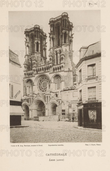 View of the Cathedral of Laon, France, Cathédrale, Laon (Aisne), page, photomechanical print, inscription: 'Reproduction interdite.', number: 'Pl. VI.', maker: Jules Royer, maker: Augustin Boutique, Douai, c. 1891 - in or before 1896, paper, collotype, photoprint, height 161 mm x width 112 mm, Print on fifth unnumbered page after page 4., church (exterior), Laon Cathedral, A sepia-toned photograph showing a large Gothic cathedral façade with two tall, ornate towers rising above a detailed front including arched doorways, a large circular rose window, decorative columns, and sculpted elements; cobblestone street in front of the cathedral leads past adjacent multi-story buildings with shuttered windows and shopfronts, one with an awning and another with a dark wooden paneled exterior; a few small figures stand near the base of the cathedral by a wall plastered with posters; the sky appears plain and light in tone above the scene.