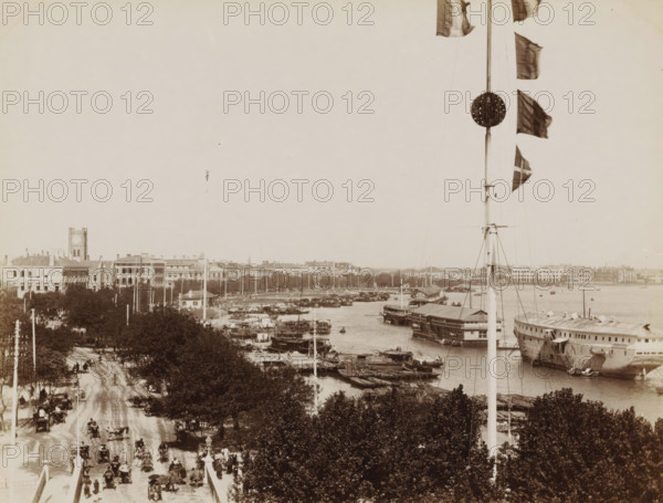 View of the Bund waterfront with three opium ships in Shanghai, album page, photograph, Part of Album with 50 photographs of a journey through Southeast Asia., Shanghai, c. 1860 - c. 1900, photographer, paper, albumen print, height 205 mm x width 271 mm, harbour, A sepia-toned riverside scene showing a tall flagpole with several flags along its length and a circular ornament near the top, a busy waterfront with many small boats and larger moored vessels, a wide tree-lined street filled with horse-drawn carriages and pedestrians, rows of multi-story buildings and a tower with a clockface visible among them, and dense foliage in the foreground.
