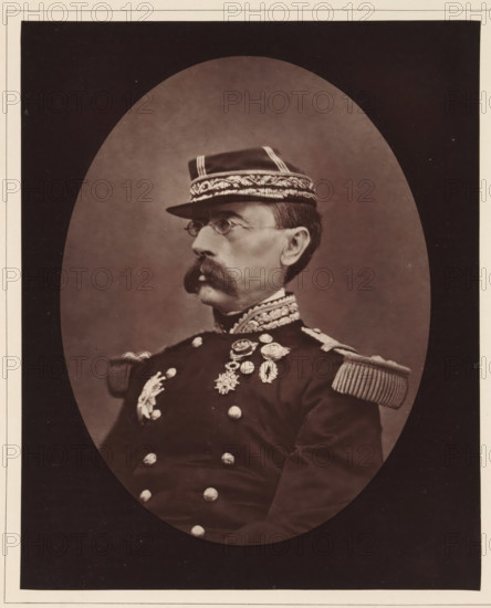 Louis-Leon-Cesar Faidherbe. Ne a Lille, le 3 juin 1818, Portrait of Louis Léon César Faidherbe, page, photomechanical print, inscription: '126, boul. Magenta.-Paris.', photographer: Étienne Carjat, cliché maker: Goupil & Cie., c. 1876 - c. 1879, paper, Woodburytype, Woodburytypie, height 230 mm x width 186 mm, Person, Louis Léon César Faidherbe, commander-in-chief, general, marshal, (military) uniforms, A sepia-toned oval portrait of a man in a formal military uniform shown in profile, facing left, wearing a peaked cap with ornate embroidered band and stripes, small round spectacles, a large handlebar mustache, an embroidered high collar, epaulettes with fringe on the shoulders, and a row of decorative medals and ornate buttons on the chest; the portrait is set against a plain backdrop and surrounded by a dark mat with a light border.