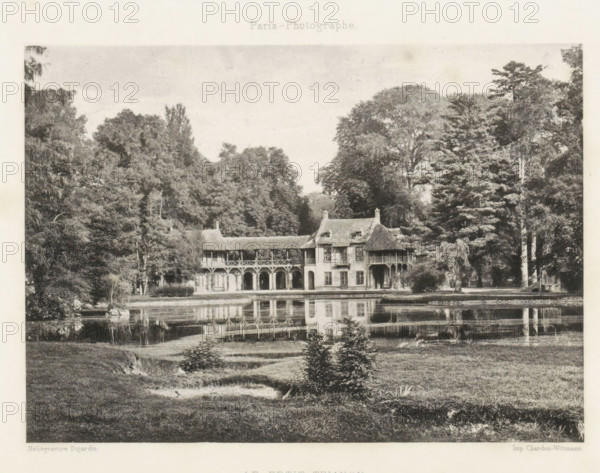 View of Le Hameau de la Reine at Versailles, Le Petit Trianon, page, photomechanical print, Versailles, cliché maker: Dujardin, France, printer (person): Chardon-Wittmann, c. 1881 - in or before 1891, photographer, printer (person), paper, photoaquatint, height 122 mm x width 170 mm, Print on endpaper., farm (building), village, architectural folly, Le Hameau de la Reine, A wide black-and-white scene shows a two-story building with arched colonnades on the ground level and a covered upper gallery, steeply pitched roofs with dormer windows, and a small turreted section, set at the edge of a reflective body of water; dense trees and tall foliage surround the building on both sides, and the water in front mirrors the arches and roofline, while grassy grounds with small shrubs and a gentle slope occupy the foreground.