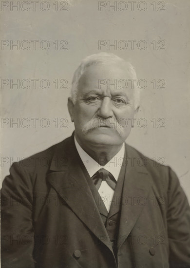 Portrait of an older man with a mustache, in dark clothing, photograph, in dark clothing., photographer: Gerschel aîné, Strasbourg (France), 1890 - 1898, paper, gelatin silver print, developed gelatin silver print, height 190 mm x width 140 mm, Period, 1890 - 1940, A close-up portrait of an older man with light hair and a thick white mustache, wearing a dark suit jacket over a waistcoat and a light-colored shirt with a necktie; his face is centered and shows visible skin texture and wrinkles, with neutral expression and eyes looking forward, and the background is a plain, slightly textured light surface.