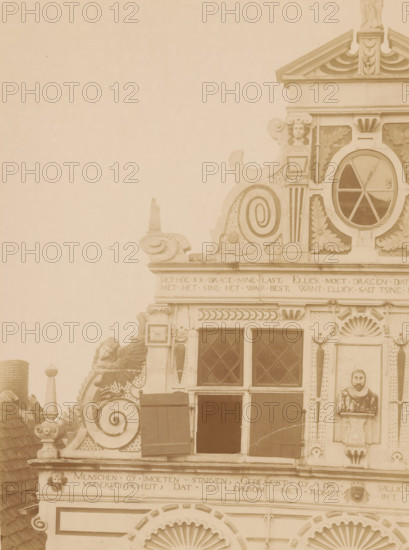 Facade of Friesestraat 9 in Coevorden, photograph, annotation: '18', annotation: 'Coevorden', Coevorden, 1890 - 1910, photographer, Attributed to, paper, pasteboard, albumen print, height 224 mm x width 168 mm, façade (of house or building), A sepia-toned photograph of an ornate building facade showing decorative stonework and carved ornaments concentrated on the upper portion, with a triangular pediment at the top, a round window with radial muntins set within a carved surround, scroll-shaped volutes, leaf and shell motifs, and a small sculpted face near the roofline; below are rectangular diamond-paned windows with wooden shutters, a carved bust set into a niche on the right, rows of horizontal friezes with carved borders, and ornamental finials and relief faces integrated into the masonry.