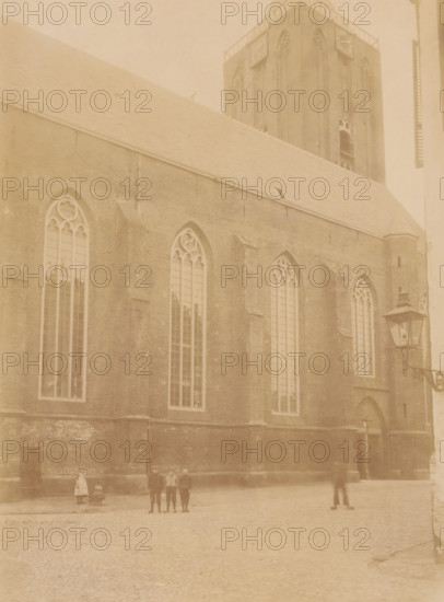View of the Great or Saint Stephen's Church in Hasselt, photograph, annotation: 'Hasselt, NH Church, Sept 1904', Hasselt (Overijssel), 1904, photographer, Attributed to, paper, pasteboard, albumen print, height 225 mm x width 169 mm, church (exterior), street (city(-scape) with figures, staffage), A large brick building with tall arched windows and ornate tracery fills most of the scene, showing a steep roof and a taller tower rising behind it; a street lamp mounted on a wrought bracket stands near a doorway in the building; a cobbled open area occupies the foreground with several small figures standing or walking and one figure near a small wheeled cart.