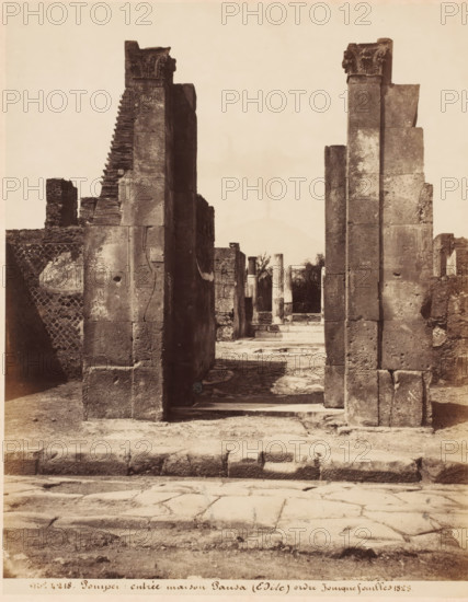 Entrée maison Pansa (Edile) ordre ionique fouillés 1823, Remains of the Casa di Pansa in Pompeii, Italy, Pompei, photograph, collector's mark: 'VOSMAER', number: 'nro. 4218.', photographer: attributed to Giorgio Sommer, Pompeii, 1857 - 1875, Giorgio Sommer, photographer, Attributed to, pasteboard, paper, albumen print, height 306 mm x width 404 mm, urban housing, ruin of a building, architecture, landscape with ruins, Casa di Pansa, A sepia-toned photograph showing a ruined stone structure with two tall, rectangular pillars in the foreground framing a view into an interior space with additional columns and fragmented walls; the pillars have weathered surfaces and ornamental capitals at their tops, and stepped masonry is visible on the left pillar; the ground in front shows a worn stone pavement and a low raised curb, while inside the framed opening there are remnants of fluted columns and scattered architectural debris with vegetation visible beyond; surrounding walls display varying t...
