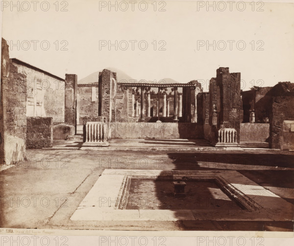 Casa del fauno, Remains of the House of the Faun at Pompeii, Pompeii, photograph, inscription: 'kns', inscription: 'B. hd technique', number: '48', number: 'No. 1269.', photographer: attributed to Giorgio Sommer, 1857 - 1875, Attributed to, pasteboard, paper, albumen print, height 319 mm x width 480 mm, urban housing, ruin of a building, architecture, landscape with ruins, A sepia-toned photograph showing the ruins of a stone building with fragments of walls and columns framing a central courtyard area; in the foreground a rectangular sunken basin with a small pedestal sits in shadow, bordered by pale stone edging, while a paved surface extends toward the midground where battered column drums and short fluted column bases rest atop a low wall; beyond this a row of taller columns supports an entablature with decorative molding, and remnants of plastered walls with door openings and niches rise on either side; the stone surfaces display rough texture and weathering, and the distant backg...