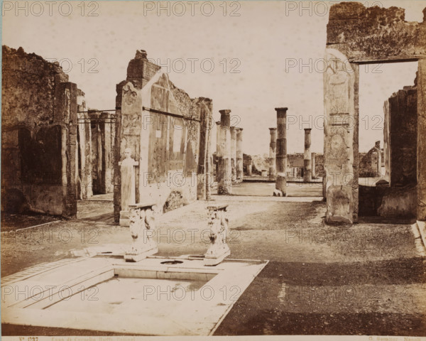 Remains of Cornelio Rufo's house in Pompeii, Casa di Cornelio Ruffo Pompei, photograph, collector's mark: 'VOSMAER', number: 'No. 1237.', photographer: Giorgio Sommer, Pompeii, 1857 - 1875, pasteboard, paper, albumen print, height 315 mm x width 420 mm, urban housing, ruin of a building, architecture, landscape with ruins, Casa di Cornelio Rufo, A sepia photograph shows an open archaeological site with weathered stone walls and tall fluted columns arranged in rows across a dirt courtyard. In the foreground there is a rectangular sunken basin with a decorative edge and two ornate stone supports with sculpted motifs placed on its far side. Ruined doorways and fragmented wall panels with patches of plaster and carved reliefs frame the view on either side, and a freestanding stone bust is mounted on a short pedestal near one of the walls. The ground is uneven with scattered stones and the sky above is pale and empty.
