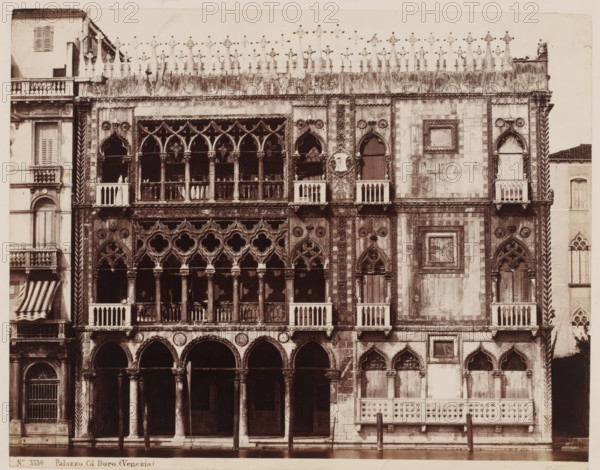 View of Palazzo Cà d'Oro in Venice, Italy, Palazzo Cà Doro. (Venezia), photograph, number: '46', inscription: 'Venetie', collector's mark: 'RICH SCHOOL FOR ART HANDBOOK, GROUP', number: 'No. 3530.', inscription: 'I', photographer: attributed to Giorgio Sommer, Venice, 1857 - 1914, Attributed to, pasteboard, paper, albumen print, height 319 mm x width 480 mm, hôtel, i.e. small palace in city, Ca' d'Oro, A sepia-toned photograph of an ornate stone facade facing water, with a ground-level arcade of rounded arches supported by columns, above which sit rows of Gothic windows with pointed arches and intricate tracery, some windows opening to small balustraded balconies. The upper cornice is topped by a decorative crenellated parapet with sculpted finials, and the facade surface displays patterned stonework, carved medallions, and framed panels with relief details. Flanking sections show vertical twisted columns and narrow windows with shutters, while the lower edge of the building meets a ca...