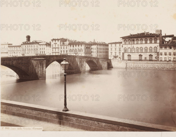 Ponte della Grazia. (Firenze), View of the Ponte della Grazia over the Arno in Florence, Italy, photograph, address: 'SOMMER & BEHLES, ROMA E NAPOLI', number: 'No. 1843.', address: 'DEPÔT A FLORENCE, J. BRECKER, VIA MAGGIO 15', photographer: Sommer & Behles, Florence, 1867 - 1874, Tuscany, pasteboard, paper, albumen print, albumendruk, height 307 mm x width 381 mm, landscape with bridge, viaduct or aqueduct, river, Arno, Ponte alle Grazie, A wide sepia-toned view of a stone arched bridge crossing a calm river with multiple evenly spaced arches; buildings with rows of windows and decorative façades line the far bank behind the bridge, including a larger multi-story building with round-topped windows; a decorative street lamp on a tall fluted post stands in the foreground on a riverside parapet made of brick and stone; the water surface is smooth and reflective, and the sky above is pale and largely empty.