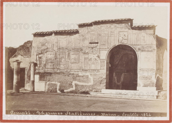 Pompei. Thermes Stabiennes - Bains - fouille 1824, Exterior of the Stabian thermal baths in Pompeii, photograph, inscription: '11', collector's mark: 'VOSMAER', photographer: attributed to Giorgio Sommer, Pompeii, 1857 - 1914, Giorgio Sommer, photographer, Attributed to, pasteboard, paper, albumen print, height 106 mm x width 154 mm, height 168 mm x width 206 mm, ruin of a building, architecture, public baths, Terme Stabiane, A sepia-toned photograph shows an ancient stone façade with decorative carved panels and a tiled roof edge above. An arched dark entrance is visible on the right side with steps leading up to it. The wall surface displays areas of smoother plaster alongside rougher exposed masonry and decorative reliefs including framed panels and draped motifs. Two freestanding columns with simple capitals stand to the left in front of the wall, and low rectangular stone blocks and bases are scattered near the base of the structure. The ground in front appears flat and worn. A na...
