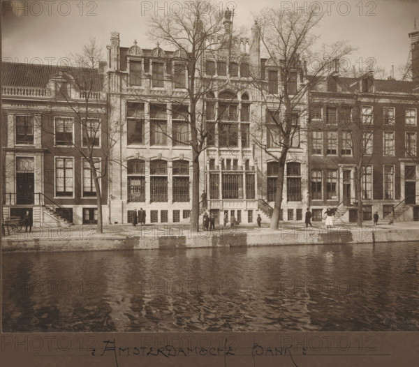 Facade of Herengracht 597 - 601 in Amsterdam, former Amsterdamsche Bank, photograph, annotation: 'Amsterdamsche Bank', annotation: 'Amsterdamsche Bank Heerengracht A'dam No 8, Architect Ed. Cuypers, Herengracht no. 8', inscription: 'Architect, Ed: Cuypers, Amsterdam', number: '1319, 164a', photographer: Fidel Carl Albert Greiner, Amsterdam, photographer: Albert Greiner, 1902 - 1930, Fidel Carl Albert Greiner, Albert Greiner, photographer, paper, pasteboard, daylight gelatin silver print, height 218 mm x width 276 mm, height 296 mm x width 420 mm, bank, street (city(-scape) with figures, staffage), façade (of house or building), Herengracht (Amsterdam), Amsterdamsche Bank, A row of tall buildings with ornate facades and large windows lines a tree-lined canal, with bare-branched trees standing in front of the central building and casting thin shadows on the stone sidewalk, decorative ironwork covering several lower windows and entrances, stone steps leading up to doorways, people standin...