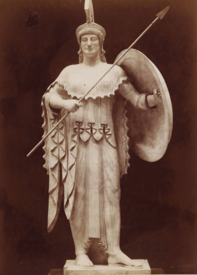 Sculpture of Pallas Athena, from the temple in Aegina, Art Grec. - Athenée provenant du Temple d'Egine Musée de Munich, photograph, name: 'A. GIRAUDON EDITOR 15. R. BONAPARTE. PARIS', inscription: 'pl 4 style k.', number: 'T 10', photographer: Adolphe Giraudon, publisher: Adolphe Giraudon, Paris, c. 1875 - c. 1900, Adolphe Giraudon, photographer, publisher, paper, pasteboard, albumen print, height 258 mm x width 189 mm, sculpture, (story of) Minerva (Pallas, Athena), protective weapons: shield, helved weapons, polearms (for striking, hacking, thrusting): lance, A full-length marble statue of a robed female figure wearing a crested helmet, holding a long spear diagonally across her body and supporting a large round shield at her side, with a scalloped edged cloak draped over her shoulders and detailed folds and decorative elements on the dress, standing barefoot on a rectangular plinth against a dark background.