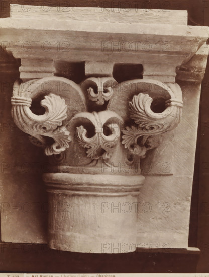 Capital with acanthus leaves, Art Roman - Charlieu (Loire) - Chapiteau., photograph, collector's mark: 'Dagteeken- en Kunstambacht- school voor Meisjes Amsterdam', name: 'A. GIRAUDON ÉDITEUR 15. R. BONAPARTE. PARIS', collector's mark: 'INSTITUUT VOOR KUNST-NIJVERHEIDSONDERWIJS GABRIËL METSUSTRAAT No. 16, AMSTERDAM', number: 'T 123', photographer: Adolphe Giraudon, Paris, c. 1875 - c. 1900, paper, pasteboard, albumen print, height 259 mm x width 254 mm, acanthus, ornament, capital (, column, pillar), A close-up view of a carved stone capital atop a fluted column, featuring symmetrical volute shapes with carved acanthus-like leaves and spiral scrolls, a broad abacus above with layered molding, weathered stone texture and surface cracks, and shadowed recesses between the decorative elements.