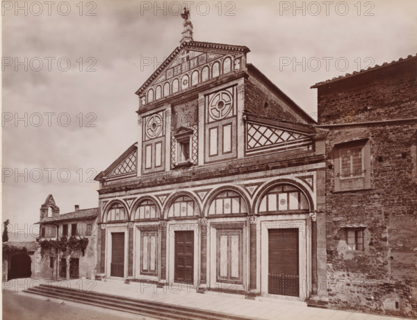 Chiesa di S. Miniato di stile greco romanzo, anteriore al mille, Façade of the San Miniato al Monte in Florence, Italy, Firenze, photograph, number: '113', number: '3031.', photographer: Giacomo Brogi (possibly), Florence, publisher: attributed to Edizioni Brogi, 1864 - 1881, Tuscany, Attributed to, pasteboard, paper, albumen print, height 318 mm x width 445 mm, church (exterior), S. Miniato, A large stone building façade with geometric and arched decorative panels, tall doorways set into framed rectangular bays, and a tiered upper section featuring circular motifs and patterned panels; a central niche with a sculpted figure flanked by painted or carved figures sits above the middle doorway, and a triangular pediment tops the composition with ornamental detailing and a statue at its peak. To the right, an adjoining stone wall with small windows and a tiled roof contrasts with the patterned façade, while to the left a smaller building with shuttered windows, a tiled roof, and an arched ...