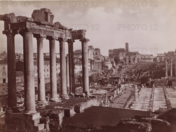 Fôro Romano, Roman Forum with Temple of Saturn in Rome, Italy, Roma, photograph, number: '103.', number: '3643.', photographer: Giacomo Brogi (possibly), Rome, publisher: attributed to Edizioni Brogi, Florence, 1864 - 1881, Tuscany, Attributed to, pasteboard, paper, albumen print, height 317 mm x width 445 mm, ruin of a building, architecture, landscape with ruins, Roman Forum, Temple of Saturn, A wide sepia-toned panorama of ancient ruins dominated on the left by a row of tall classical columns with carved capitals and a partially intact entablature, standing on heavy bases above worn stone foundations, with scattered broken masonry and rubble at their feet; behind and between the columns are low buildings with tiled roofs and simple facades, and further back a domed structure and a taller multi-tiered tower rise above other classical and baroque façades; the central and right areas show an expanse of archaeological remains including fragmented walls, paved pathways, rows of short rui...