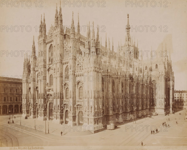 View of the Cathedral of Milan, Italy, La Cattedrale, Milano, photograph, number: '3818a.', collector's mark: 'VOSMAER', Milan, publisher: Giacomo Brogi, Florence, 1856 - 1881, Giacomo Brogi, photographer, publisher, Tuscany, Lombardy, pasteboard, paper, albumen print, height 314 mm x width 420 mm, church (exterior), Cathedral (Milan), A large ornate cathedral façade fills most of the image, showing tall pointed spires, intricate stone carvings, arched windows, and numerous sculpted figures and decorative elements on multiple levels; broad steps lead up to several arched entrances at street level, where small groups of people and a few lone figures are scattered along the sidewalks and near lampposts; a tram or streetcar is visible beside the building and tracks run along the adjacent streets, with clusters of pedestrians walking across open paved areas; to the left and right low multi-story buildings frame the scene, and the overall image has a pale, sepia-toned appearance.