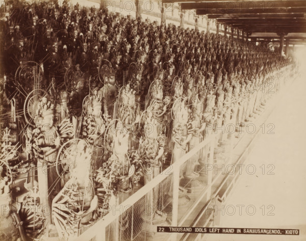 22. Tnousand Idols left hand in Sanjiusangendo.- Kyoto, Wooden statues of Kannon in the Sanjusangendo Temple, Kyoto, photograph, number: '9.', c. 1895 - c. 1915, photographer, Kinki, paper, pasteboard, albumen print, height 210 mm x width 269 mm, height 243 mm x width 329 mm, A sepia-toned photograph showing a long row of similar ornate statues arranged closely together on a raised platform behind a wire mesh railing, each statue featuring detailed headdresses, multiple arms, and circular halo-like structures, with the figures extending into the distance under a ceiling supported by beams and posts, and bright overexposed light on the far right side obscuring details.