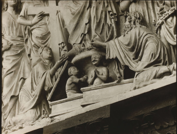Fürstentor, Tymphanon, Maria u. Johannes Fri, Detail of the tympanum of the Fürstenportal in Bamberg Cathedral, album page, photograph, This photo is part of an album., inscription: 'Kunsthist. Seminar, Marburg (Lahn), Photogr. Abteilung, Vervielfältigung, untersagt.', number: '114', Bamberg, 1900 - c. 1920, photographer, Bavaria, paper, baryta paper, gelatin silver print, developing gelatin silver print, height 180 mm x width 235 mm, church (exterior), Bamberg Cathedral, A carved stone relief shows several draped figures in a close arrangement, with detailed folds in flowing garments and textured hair. One figure on the right is kneeling and leans forward with an outstretched arm, hair falling in wavy locks over the shoulder. Two small childlike figures occupy a lower recessed area, one facing upward with hands together and a smiling expression, the other reaching toward the first while looking up. A robed figure to the left gestures with an open hand and holds a rectangular object an...