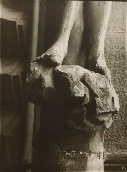 Detail of the Adamspforte in the cathedral of Bamberg, Adamspforte, Eva, Sockel, album page, photograph, This photo is part of an album., number: '59', inscription: 'Kunsthist. Seminar, Marburg (Lahn), Photogr. Abteilung, Vervielfältigung, untersagt.', Bamberg, 1900 - c. 1920, photographer, Bavaria, paper, baryta paper, gelatin silver print, developing gelatin silver print, height 239 mm x width 178 mm, church (exterior), Bamberg Cathedral, A close-up black-and-white photograph of two stone feet resting on a rough textured rock surface, showing worn and chipped edges and visible surface irregularities; the lower legs extend upward with smooth but weathered contours, and surrounding background areas include vertical stone columns and a rock wall with coarse masonry, all rendered in soft contrasts of light and shadow.
