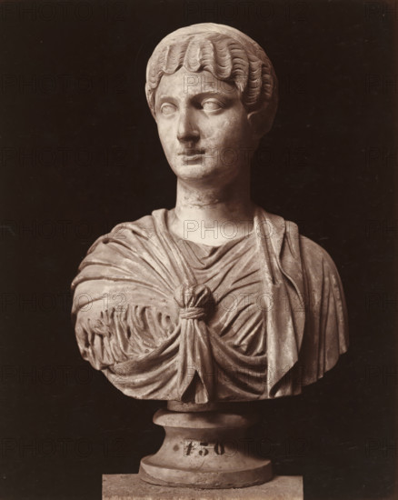 Museo di Napoli, Imperatrice, Bust, album page, photograph, This photo is part of an album., number: '7546', workshop stamp: 'Giorgio Sommer, Largo Vittoria, Napoli', photographer: Giorgio Sommer, Naples, 1874 - in or before 1879, paper, albumen print, height 253 mm x width 206 mm, Person, Antoninus Pius (Emperor of the Roman Empire), sculpture, classical history, A stone bust of a person shown from the chest up with short, wavy hair and a neutral facial expression, wearing draped garments gathered at the chest with a knot and folds, mounted on a round pedestal.