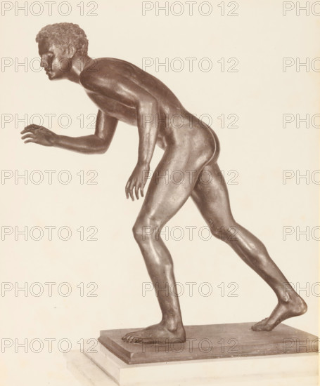 Museo di Napoli Discobolo, Bronze sculpture of an athlete, album page, photograph, This photo is part of an album., workshop stamp: 'Giorgio Sommer, Largo Vittoria, Napoli', number: '1508', photographer: Giorgio Sommer, Naples, 1874 - in or before 1879, paper, albumen print, height 252 mm x width 203 mm, sculpture (bronze, arts), athletics, gymnastics (sportsman, player, etc.), A photograph of a bronze male figure in a forward-leaning stride pose shown from the side, with a detailed head of short curly hair and a focused facial expression, one arm extended forward with slightly curled fingers and the other arm hanging down, musculature and body contours visible along the torso, hips, thighs, and calves, one foot planted on a rectangular base and the other foot lifted on its toes, the sculpture resting on a stepped plinth against a pale, neutral background.