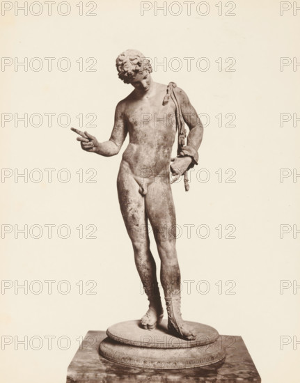 Sculpture of Narcissus, Museo di Napoli Narciso, album page, photograph, This photo is part of an album., number: '1535', workshop stamp: 'Giorgio Sommer, Largo Vittoria, Napoli', photographer: Giorgio Sommer, Naples, 1874 - in or before 1879, paper, albumen print, height 249 mm x width 201 mm, sculpture, (story of) Narcissus, A grayscale photograph of a full-length classical statue of a nude male figure standing on a round stepped pedestal, the figure leaning slightly with weight on one leg, curly hair, head tilted downward, left arm bent with hand pointing outward, right arm resting at the side holding a draped cloth or sash that falls over the shoulder, visible detailed musculature and worn surface texture, one foot bare and the other wearing a laced sandal, the background plain and light.